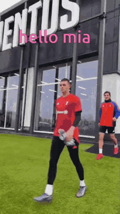 A Man In A Red Shirt Is Walking In Front Of A Building That Says " Hello Mia " GIF