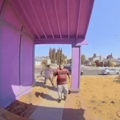 A Man In A Red Shirt Is Walking On A Sidewalk Under A Purple Roof GIF