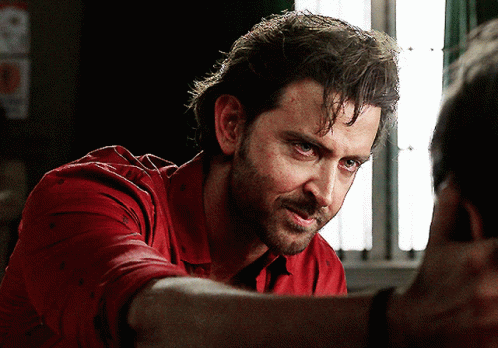 A Man In A Red Shirt Looks Down At Something GIF