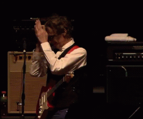 A Man In A Red Shirt Plays A Guitar On Stage GIF