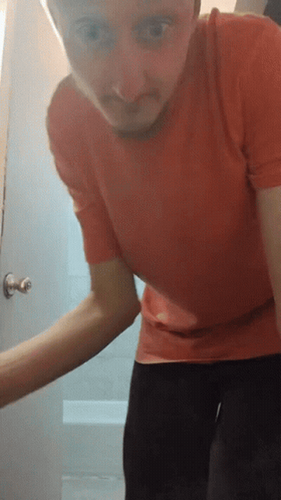 A Man In A Red Shirt Stands In Front Of A Door GIF
