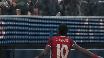 A Man In A Red Shirt Stands In Front Of A Sign That Says Us GIF