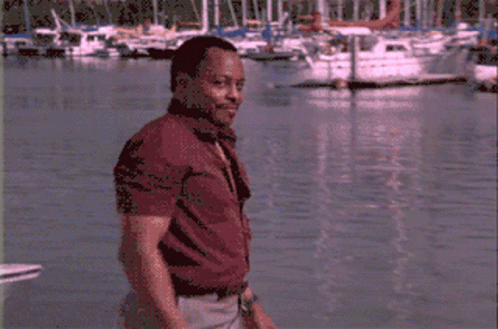 A Man In A Red Shirt Stands In Front Of Boats GIF