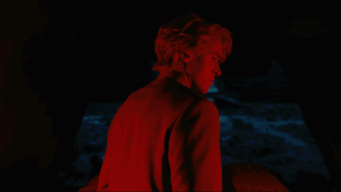 A Man In A Red Shirt Stands In The Dark GIF