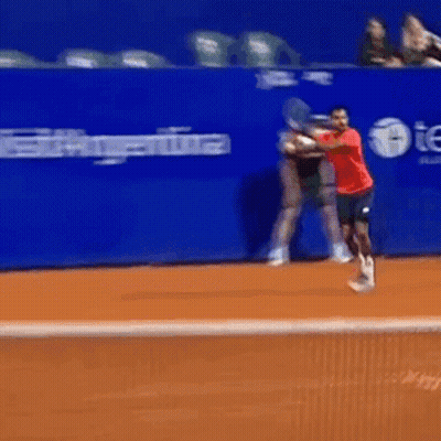 A Man In A Red Shirt Swings A Tennis Racquet On A Tennis Court GIF