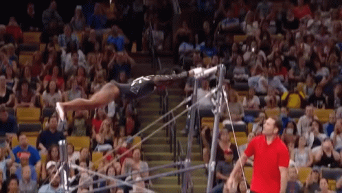 A Man In A Red Shirt Watches A Gymnast Perform On A Bar GIF