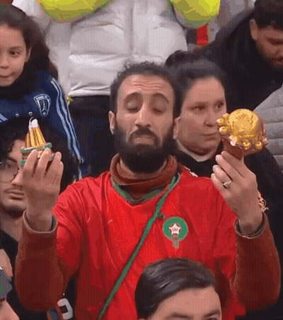 A Man In A Red Shirt With A Green Star On It Holds A Gold Object GIF