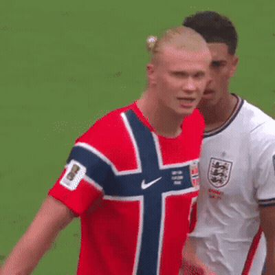 A Man In A Red Shirt With A Norwegian Flag On It Is Standing Next To Another Man In A White Shirt . GIF