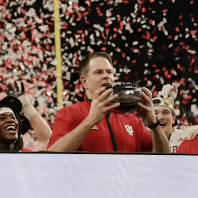 A Man In A Red Shirt With The Letter U On It Holds A Football GIF