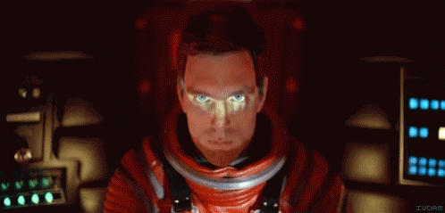 A Man In A Red Space Suit Is Sitting In A Dark Room . GIF