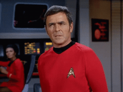 A Man In A Red Star Trek Uniform Stands In Front Of A Computer Screen GIF