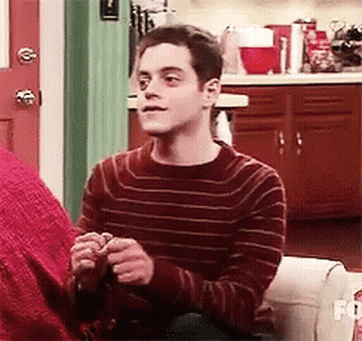A Man In A Red Striped Sweater Is Sitting On A Couch Holding A Knitting Needles . GIF