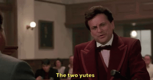 A Man In A Red Suit And Bow Tie Is Standing In Front Of A Microphone And Says The Two Yutes . GIF