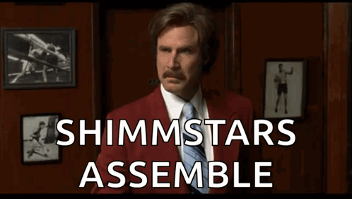 A Man In A Red Suit And Tie Is Holding A Fist In Front Of A Sign That Says Shimmstars Assemble . GIF