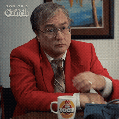 A Man In A Red Suit And Tie Is Sitting At A Table With A Cup That Says Boom GIF