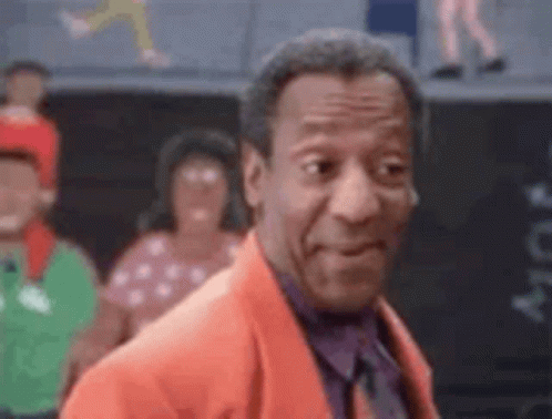 A Man In A Red Suit And Tie Is Standing In Front Of A Crowd Of People . GIF