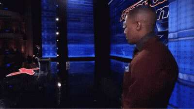 A Man In A Red Suit And Tie Stands In Front Of A Sign That Says America 'S Got Talent GIF