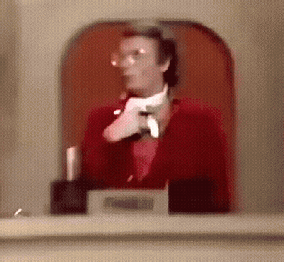 A Man In A Red Suit And White Tie Is Standing In Front Of A Glass Door . GIF