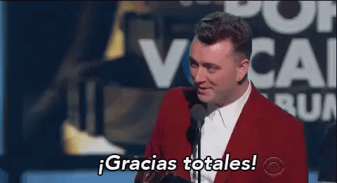 A Man In A Red Suit Is Giving A Speech In Front Of A Microphone And Says Gracias Totales . GIF