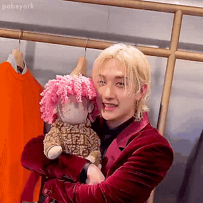 A Man In A Red Suit Is Holding A Stuffed Sheep With Pink Hair . GIF