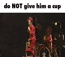 A Man In A Red Suit Is Jumping In The Air In Front Of A Drum Set With The Caption Do Not Give Him A Cup GIF