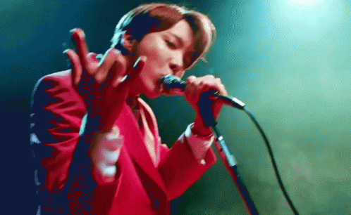 A Man In A Red Suit Is Singing Into A Microphone GIF