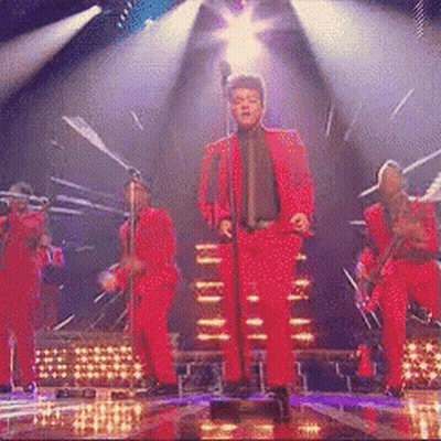 A Man In A Red Suit Is Singing Into A Microphone On A Stage GIF