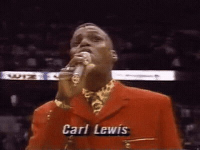 A Man In A Red Suit Singing Into A Microphone With The Name Carl Lewis Written On His Chest GIF