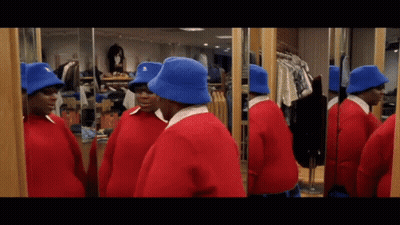 A Man In A Red Sweater And Blue Hat Looks At Himself In The Mirror GIF