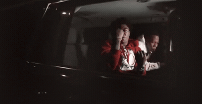 A Man In A Red Sweater Is Sitting In The Back Seat Of A Car . GIF