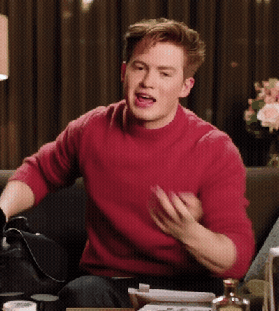 A Man In A Red Sweater Is Sitting On A Couch And Talking GIF