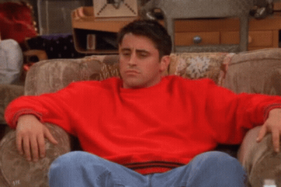 A Man In A Red Sweater Is Sitting On A Couch With The Words Ah-Ha Written On His Chest . GIF