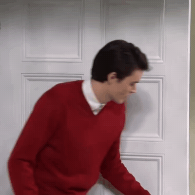 A Man In A Red Sweater Is Standing In Front Of A Door . GIF