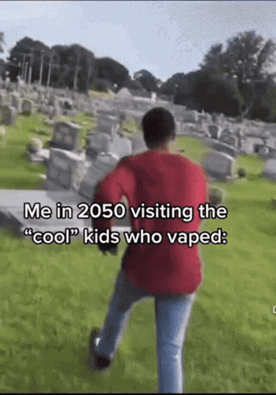 A Man In A Red Sweater Is Walking Through A Cemetery With The Caption " Me In 2050 Visiting The Cool Kids Who Vaped " GIF