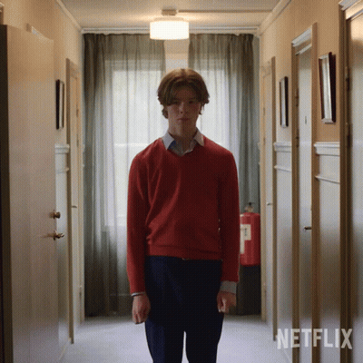 A Man In A Red Sweater Stands In A Hallway With Netflix Written On The Wall Behind Him GIF