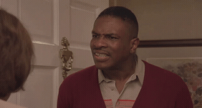 A Man In A Red Sweater Stands In Front Of A Door GIF