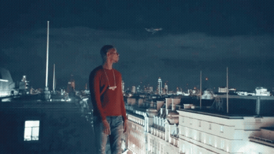 A Man In A Red Sweater Stands On The Roof Of A Building GIF