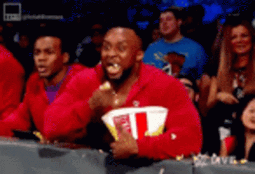 A Man In A Red Sweatshirt Is Eating Popcorn In A Crowd . GIF
