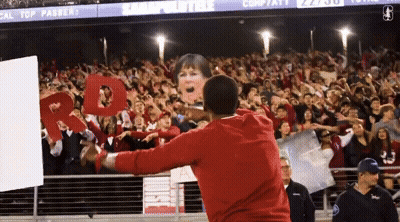 A Man In A Red Sweatshirt Stands In Front Of A Crowd Holding A Sign That Says " Cal Top Passer " GIF