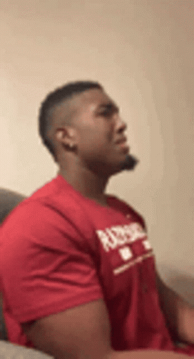 A Man In A Red T-Shirt Is Sitting On A Couch . GIF