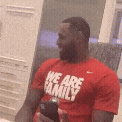 A Man In A Red T-Shirt That Says `` We Are Family '' Is Holding A Cell Phone . GIF