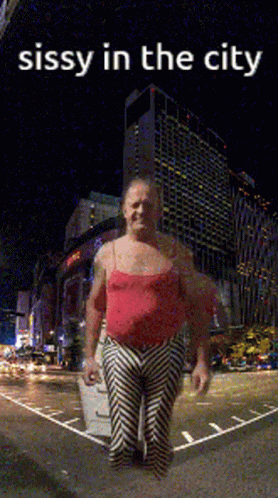 A Man In A Red Tank Top And Striped Pants Is Standing In Front Of A City At Night With The Caption Sissy In The City GIF