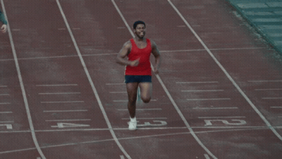 A Man In A Red Tank Top Is Running On A Track With His Arms Outstretched GIF