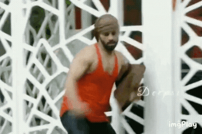 A Man In A Red Tank Top Is Standing In Front Of A White Fence . GIF