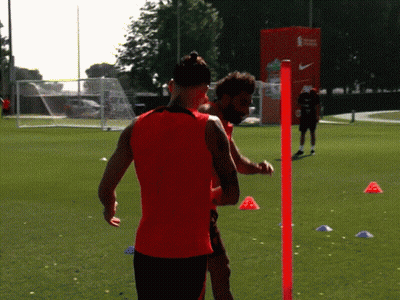 A Man In A Red Tank Top Is Standing Next To Another Man GIF