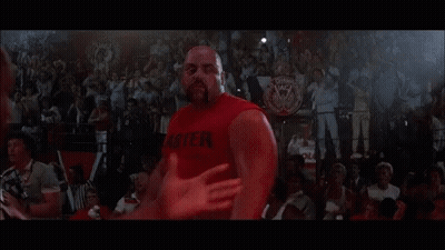 A Man In A Red Tank Top Is Standing Next To Another Man In A Wrestling Ring . GIF