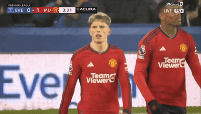 A Man In A Red Team Viewer Jersey Stands Next To Another Man On A Soccer Field GIF