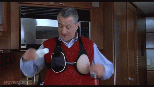A Man In A Red Vest Is Holding A Bottle In His Hands In A Kitchen .. GIF