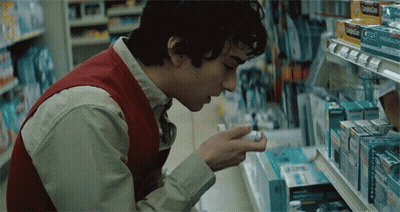A Man In A Red Vest Is Looking At A Box Of Cold Medicine In A Store GIF