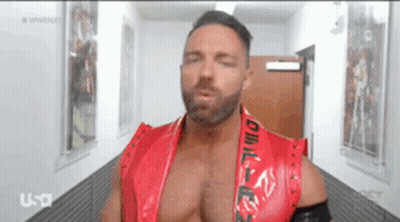 A Man In A Red Vest Is Standing In A Hallway GIF